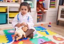 Meisje met doktersoutfit zit met een beer op de grond van een kinderopvangorganisatie.