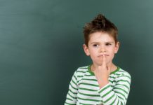 Jongen die voor een schoolbord staat en nadenkt met een vinger onder zijn mond