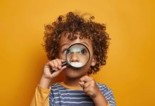 A cute little boy holding a magnifying glass, with a curious expression on his face isolated against a solid color background