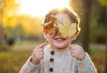 Jongen verbergt zijn ogen met twee herfstbladeren