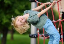 Blonde jongen hangt aan een klimrek op de kinderopvang.