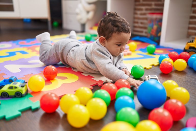 Baby kruipt op de grond tussen gekleurde speelgoedballen