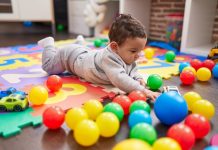 Adorable hispanic baby playing with balls lying on floor at kindergarten