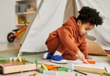 Full length portrait of cute toddler boy drawing on floor in kids room while dressed in trendy neutral outfit