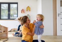 Klein meisje huilt en schreeuwt, pedagogisch medewerker houdt haar in de armen en stelt haar gerust.